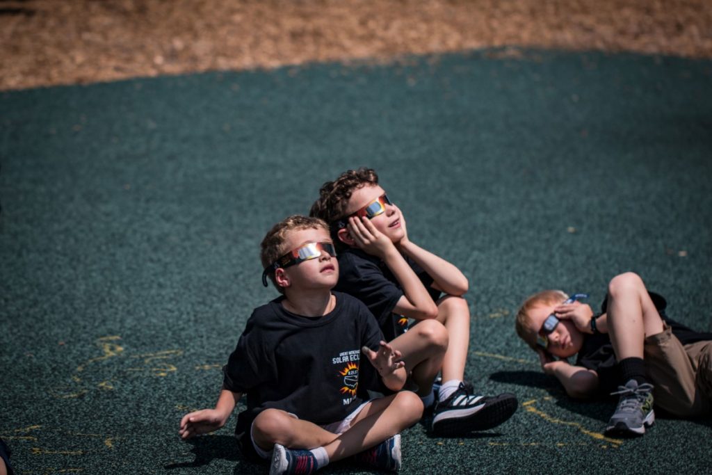 Students on a field stare at the sun wearing protective eyewear